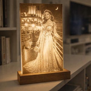 Könnte beinhalten: Sepiafarbene LED-Leuchte mit einer Frau in einem Abendkleid auf einem Schiffsdeck, mit einem Mond im Hintergrund. Die Leuchte ist auf einem rechteckigen Holzsockel montiert und erzeugt ein warmes, umgebendes Leuchten. Das Bild ist ein Porträt.