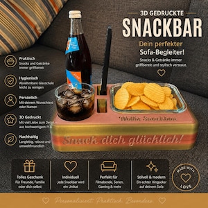 Puede incluir: Una bandeja snack bar impresa en 3D con acabado degradado, que incluye un cuenco de cristal con patatas fritas onduladas, un vaso de refresco oscuro y una ranura para el mando. La bandeja tiene grabados los textos "Wollix Snackbox" y "Snack dich glücklich!"