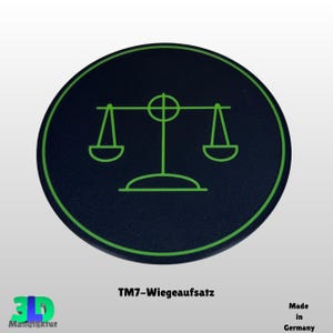 Könnte beinhalten: Ein rundes, schwarzes Objekt mit grünem Rand und einem grünen Waagensymbol in der Mitte. Der Text "TM7-Wiegeaufsatz" befindet sich darunter, und das 3D Manufaktur-Logo ist unten links. Die Worte "Made in Germany" stehen unten rechts.