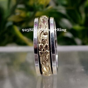 Könnte beinhalten: Ein Silber- und Gold-Spinnerring mit floralem Design. Der Ring hat eine strukturierte Oberfläche und ist aus 925er Silber.