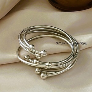 Könnte beinhalten: Ein Set aus vier silbernen Armreifen mit kleinen Kugelakzenten. 925 Silver Spinner Ring.