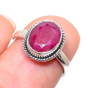 Puede incluir: Un anillo de plata con una piedra preciosa de rubí rojo. El anillo tiene una banda retorcida y un engaste de bisel.