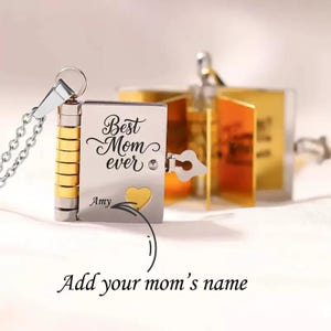 May include: A silver and gold locket necklace with the words "Best Mom ever" engraved on the front. The locket has a small gold heart and the name "Amy" below the text. The necklace is on a white background.