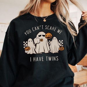 May include: Black sweatshirt with a white graphic of three ghosts holding jack-o-lanterns. The text on the sweatshirt reads 'You can't scare me I have twins'.