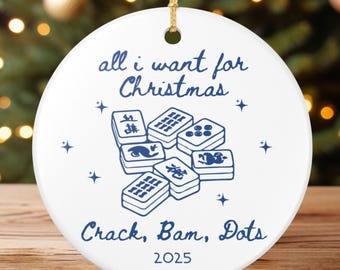 May include: White ceramic Christmas ornament with a gold string. The ornament features blue text that reads "all I want for Christmas" and "Crack, Bam, Dots" with a graphic of Mahjong tiles. The year "2025" is also printed on the ornament.