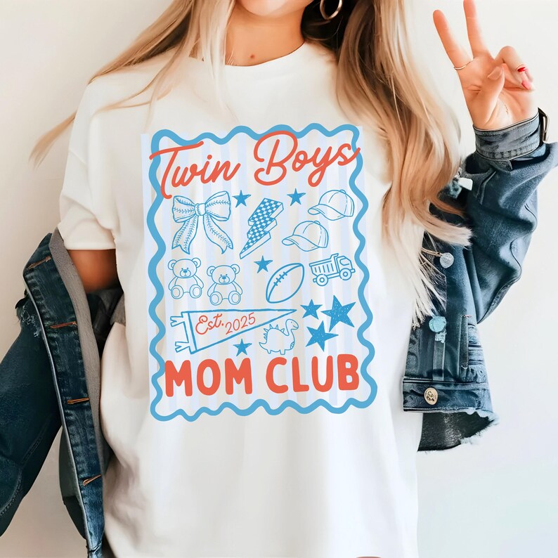 May include: White t-shirt with a blue and red graphic that reads "Twin Boys Mom Club Est. 2025." The graphic includes illustrations of a bow, lightning bolt, baseball caps, teddy bears, a football, a truck, stars, and a dinosaur.