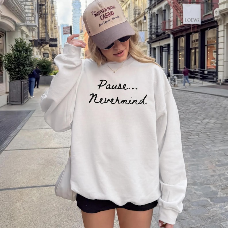 May include: A white sweatshirt with the text "Pause... Nevermind" in black script. The image also shows a tan baseball cap with the text "The Western House Casino Las Vegas, Nevada".
