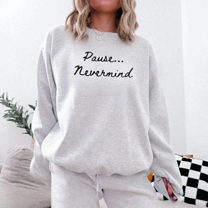 May include: A light gray sweatshirt with the text "Pause... Nevermind" in a black script. The sweatshirt is part of a matching set, and the model is wearing a necklace.