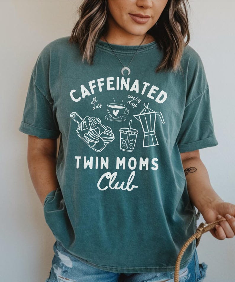 May include: Teal blue t-shirt with a white graphic design that says "caffeinated all day, every day" with images of coffee, tea, and pastries. The text "Twin Moms Club" is below the graphic.
