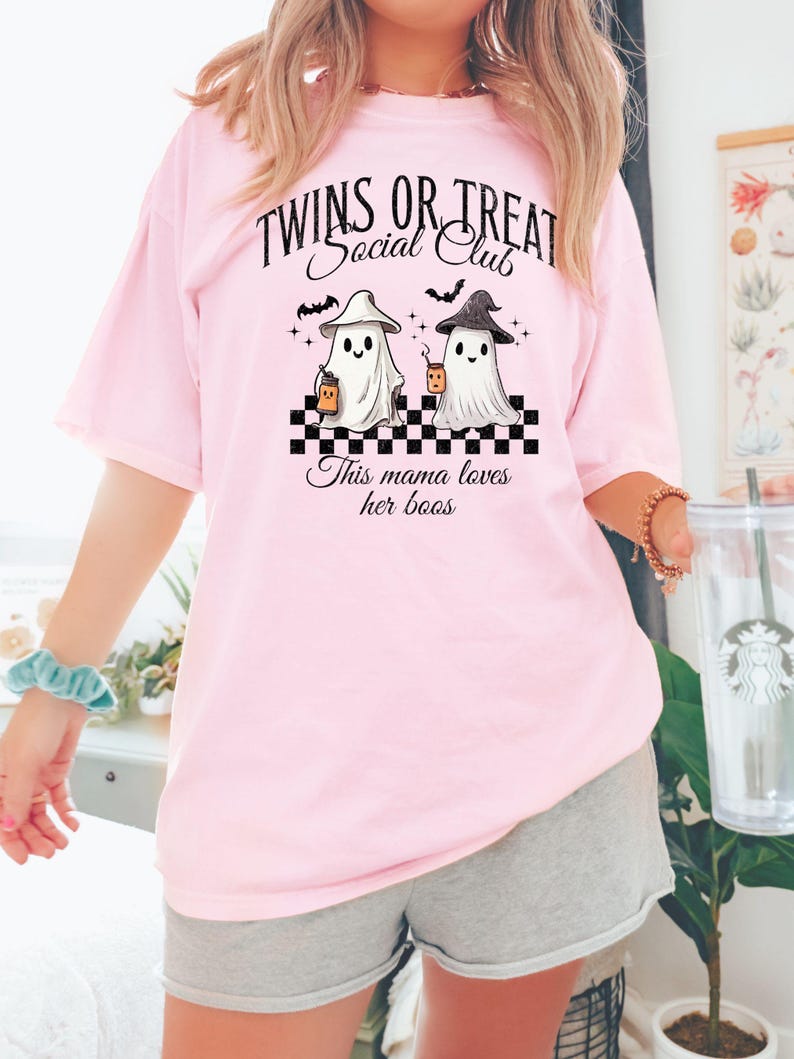 Puede incluir: Camiseta rosa con un gr&aacute;fico de dos fantasmas sosteniendo tazas y el texto "Twins or Treat Social Club" y "This mama loves her boos".