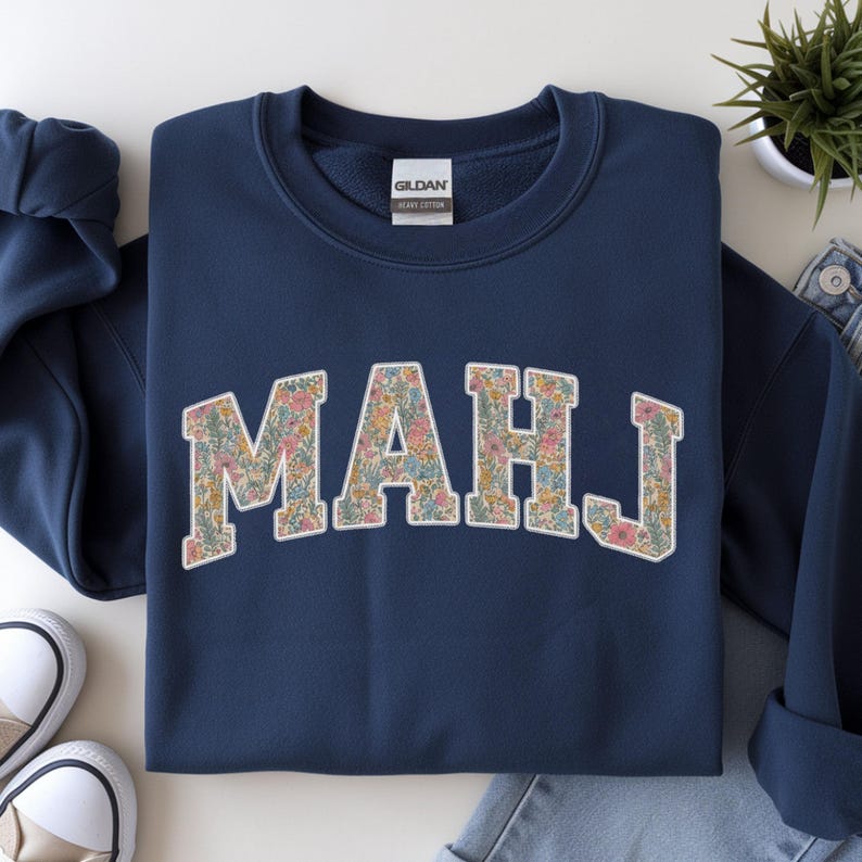 May include: Navy blue sweatshirt with the word "MAHJ" in a floral pattern. The letters are in a collegiate style, with a white outline. The sweatshirt is made of a heavy cotton material.