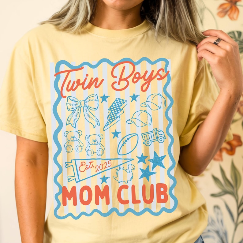 May include: Yellow t-shirt with a blue and red graphic that reads "Twin Boys Mom Club." The graphic includes illustrations of a bow, lightning bolt, baseball caps, teddy bears, a football, a truck, stars, and a dinosaur.