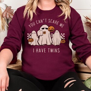 May include: Burgundy sweatshirt with a graphic of three ghosts holding jack-o-lanterns. The text on the sweatshirt reads "You can't scare me I have twins".