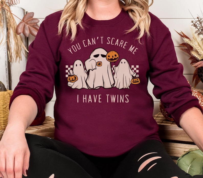 May include: Burgundy sweatshirt with a graphic of three ghosts holding jack-o-lanterns. The text on the sweatshirt reads "You can't scare me I have twins".