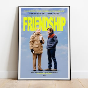 Puede incluir: Un póster enmarcado de la película "Friendship" con Tim Robinson y Paul Rudd. El título está en letras amarillas grandes. El póster presenta a dos hombres con ropa de invierno sobre un fondo de cielo azul. El texto "Men Shouldn't Have Friends" está en la parte inferior.