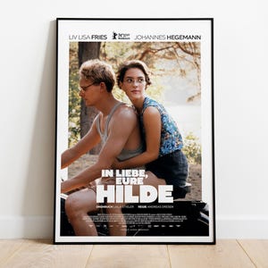 May include: A framed movie poster for "In Liebe, Eure Hilde" featuring two people on a motorcycle. The poster has the names Liv Lisa Fries and Johannes Hegemann at the top. The title is in large white letters.