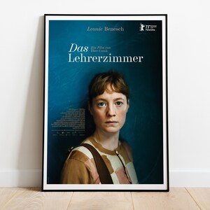May include: A movie poster for the film "Das Lehrerzimmer" directed by Leonie Benesch. The poster features a woman with short brown hair looking directly at the viewer. The background is a dark blue color.