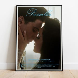Pode incluir: Um cartaz de filme emoldurado para "Priscilla" com um close-up de um casal se abraçando. O título está em script azul claro, com os nomes dos atores e do diretor abaixo. O cartaz é exibido em uma parede branca.