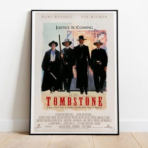 May include: A movie poster for the film "Tombstone" featuring Kurt Russell and Val Kilmer. The poster has a red and white background with the title "Tombstone" in large red letters. The tagline "Every town has a story. Tombstone has a legend." is printed below the title.