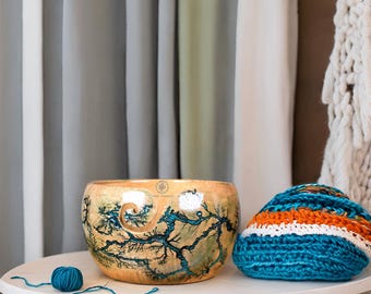 Könnte beinhalten: Eine runde Garnschale aus Holz mit naturfarbenem, hellbraunem Finish, dunkelblauen Fraktal-Brandmustern und einem spiralförmigen Ausschnitt. Neben der Schale liegen ein kleines Knäuel blaugrünes Garn und ein angehäkeltes Stück.