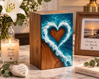 May include: A rectangular wooden cremation urn featuring a front panel with a vibrant blue ocean wave design that forms a heart shape. The natural wood grain is visible on the sides, and the front artwork displays textured white sea foam.