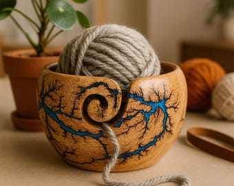 Könnte beinhalten: Eine runde Garnschale aus Holz mit natürlicher hellbrauner Oberfläche, verziert mit dunklen Fraktal-Brandmustern und leuchtend blauen Harzeinlagen. Ein spiralförmiger Ausschnitt ermöglicht das Durchführen eines hellgrauen Garnfadens.