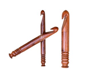 May include: Three polished brown wooden crochet hooks with a smooth finish. Each hook features a carved, ribbed handle at the base and a curved hook at the top. One hook is positioned horizontally across the others, displaying a small logo.