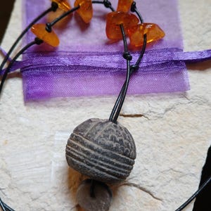 May include: A necklace with a black cord and amber beads. The necklace has a round, dark brown pendant with a textured surface.