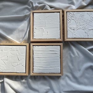 Puede incluir: Conjunto de cuatro lienzos blancos texturizados en marcos de madera. Cada lienzo tiene un diseño abstracto diferente.