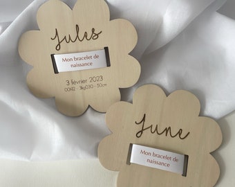May include: Two wooden flower-shaped tags with the names "Jules" and "June" engraved on them. Each tag has a white ribbon with the text "Mon bracelet de naissance" printed on it. The Jules tag also includes the date "3 février 2023" and the measurements "00h12 - 3kg030 - 50cm".
