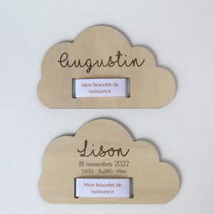 Puede incluir: Dos placas de madera en forma de nube con nombres, fechas de nacimiento y medidas grabadas. La placa superior dice "Augustin" y la placa inferior dice "Lison 18 de noviembre de 2022 15h30 - 2kg880 - 49cm". Ambas placas tienen una ranura para un brazalete.