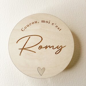 May include: A round wooden sign with the text "Coucou, moi c'est Romy" and a small heart in the center.