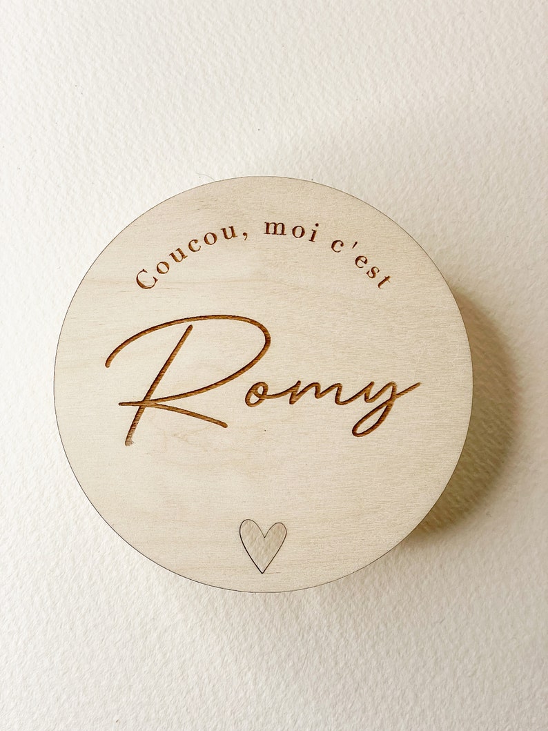 May include: A round wooden sign with the text "Coucou, moi c'est Romy" and a small heart in the center.