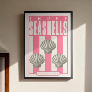 May include: A framed poster featuring the words "THREE SEASHELLS" in pink and white stripes, with three grey seashell illustrations. The text "ENHANCE CALM" is at the bottom. The poster is in a black frame.