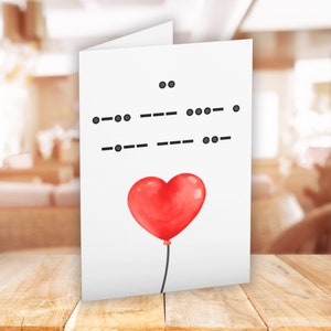 May include: A white card with a red heart-shaped balloon and a message written in Morse code. The message reads "I love you".