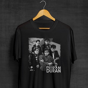 May include: Black t-shirt featuring a black and white image of the band Duran Duran. The image shows the band members in a group photo. The band's name is printed in white below the image.