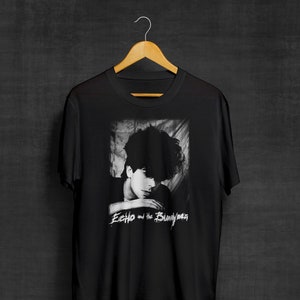 May include: Black t-shirt with a white image of a person with dark hair and the text "Echo and the Bunnymen" printed on the front.