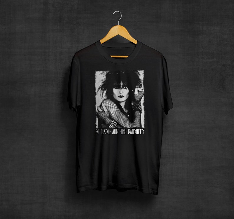 May include: Black t-shirt with a white and gray image of Siouxsie Sioux from the band Siouxsie and the Banshees. The image is in a rectangular frame with the band's name printed below it.
