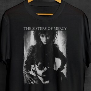 May include: Black and white photo of The Sisters of Mercy band members on a black t-shirt. The band's name is printed in white above the photo.