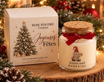 May include: A scented candle in a clear glass jar with a cork lid and a red ribbon, featuring a gnome graphic and the text Joyeux noël MARRAINE. Beside it sits a white cardboard box printed with a Christmas tree and the text Rose Poudré Création Joyeuses Fêtes.