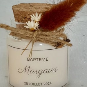 May include: A small glass jar with a cork lid, decorated with dried flowers and twine. The jar has a white label with the text "BAPTEME Margaux 28 JUILLET 2024".