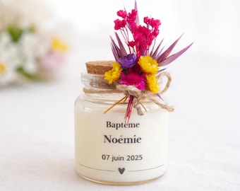 May include: A small glass jar with a cork stopper, adorned with a bouquet of pink, yellow, and purple flowers. The jar is tied with twine and features the text "Baptême Noémie 07 juin 2025" in black. A small heart is printed below the date.