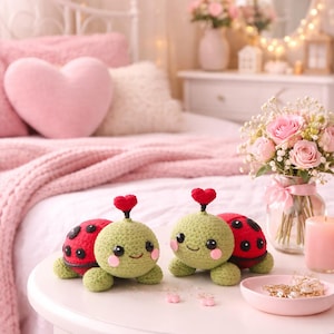 May include: Two handmade crochet turtle figurines with red and black shells and green bodies, each topped with a red heart. They sit on a white table with a pink dish of jewelry, a candle, and a bouquet of pink roses.