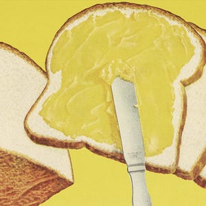 May include: A close-up of a knife spreading yellow butter on a slice of white bread. There are three more slices of bread in the background.