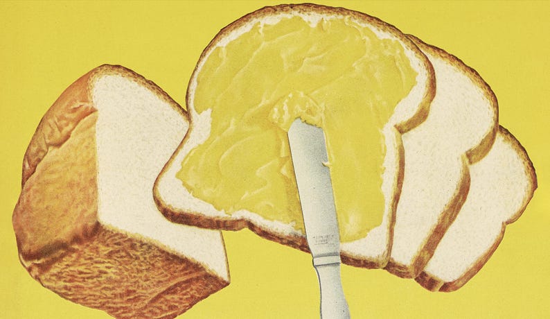 May include: A close-up of a knife spreading yellow butter on a slice of white bread. There are three more slices of bread in the background.