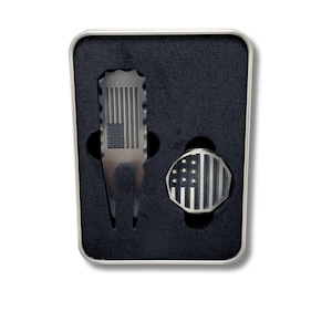 Close-up of a custom engraved golf divot tool and a ball marker, each with an American flag design, in a black foam-lined metal gift box.