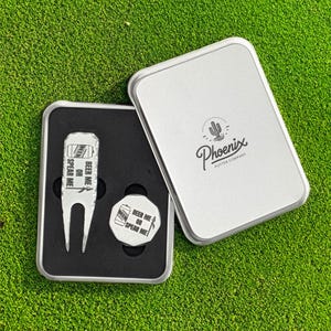 May include: A silver golf divot repair tool and ball marker set in a metal case. The tool and marker have the text "BEER ME OR SPEAR ME!". The case is silver with the Phoenix Putter Company logo.