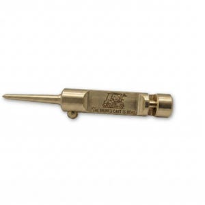 Close-up of a brass, retractable golf divot tool on a light wooden table. A brown book is blurred in the background.