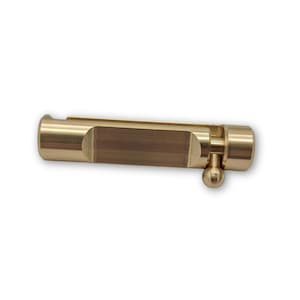 Close up of a brass divot tool with a brushed finish, featuring a round ball-shaped push button.