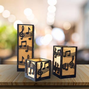 Pode incluir: Três castiçais decorativos com tema musical. As molduras de madeira preta apresentam recortes de notas musicais e pautas, envolvendo um interior bege quente. Os castiçais são de tamanhos e formatos diferentes, criando uma exibição visualmente atraente.